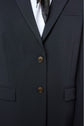 Close-up of a person wearing a veste tailleur femme in dark fabric with two buttons fastened, a white shirt underneath, and a black scarf peeking out from the collar. Only the torso area is visible.