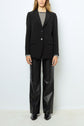 Person wearing a veste tailleur femme noire over a black and white striped sweater, black leather pants, and black shoes, standing against a plain white background.