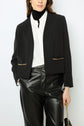 Woman wearing a microfibre noir veste courte adorned with chaînes dorées, paired with a white button-up shirt, black turtleneck, and black leather pants, holding a small black handbag. Only her lower face is visible.