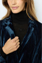A woman wearing a black turtleneck and a dark blue velvet jacket, holding the lapel with one hand. Only the lower part of her face, neck, and upper torso are visible.
