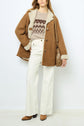 Woman in a brown shearling coat, reminiscent of a manteau mouton velours, patterned sweater, white high-waisted wide-leg jeans, brown boots, and tan crossbody bag, standing against a plain background.
