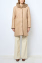 A person wears a tan shearling coat with a hood, reminiscent of a manteau agneau, paired with cream wide-leg pants and brown shoes, standing against a plain white background. Only the lower face and body are visible.