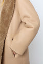 A person wearing a beige manteau peau lainée with one hand tucked into a side pocket, showing the textured fur lining and smooth leather exterior.