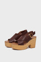 A pair of sandales compensées in rich cuir marron, featuring crisscross straps and wooden block heels (semelle en bois), with gold buckles adorning the ankle straps, set against a plain white background.