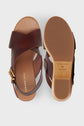 A pair of sandales compensées in cuir marron with crisscross straps, a gold buckle, and a tan sole with semelle en bois, shown from above and below on a white background.