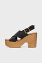 A black leather platform sandal with crisscross straps, a gold buckle, and a chunky semelle en bois heel. The sole is thick and curves upward at the toe. The background is plain white.