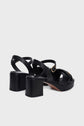 A pair of black sandales à plateforme with thick block heels, crisscross straps in luxurious cuir matelassé, and gold buckle details, fabriquées en Italie, displayed on a white background.