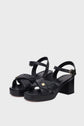 A pair of black sandales à plateforme with block heels, ankle straps, gold buckle closures, and crisscross quilted cuir matelassé straps featuring a small gold square detail on the front, fabriquées en Italie.