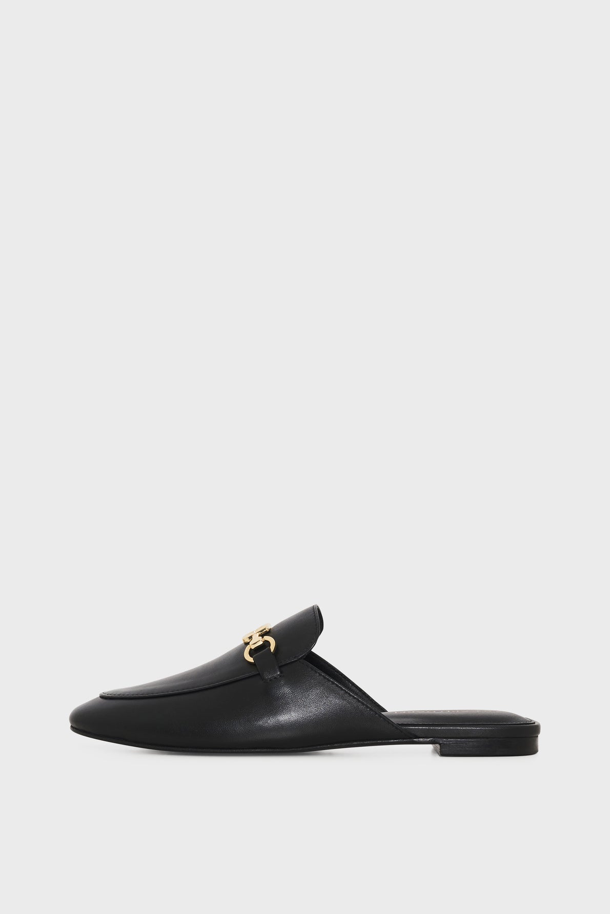 A black leather mule shoe with a flat heel and a gold decorative buckle detail on the upper, displayed against a plain white background.