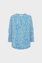 Blue blouse fluide with a white motif floral print, featuring a v-neckline and manches 7/8 with gathered cuffs, displayed on a plain white background.