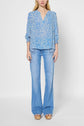 A woman wearing a blue blouse fluide à manches 7/8 with a motif floral and light blue flared jeans with front pockets and platform sandals, standing against a plain white background.
