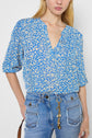 Woman wearing a blue and white motif floral blouse fluide with a V-neck and manches 7/8, paired with high-waisted blue jeans featuring front pockets and a decorative keychain.