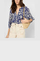 Woman wearing a blue and white blouse fluide with an imprimé graphique, paired with cream high-waisted pants and carrying a woven straw shoulder bag. Only her torso is visible; her head is partially out of frame.