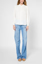 A person wearing a white long-sleeve blouse, light blue flared jeans with white side seams and front pockets, and tan platform sandals, standing against a plain background.