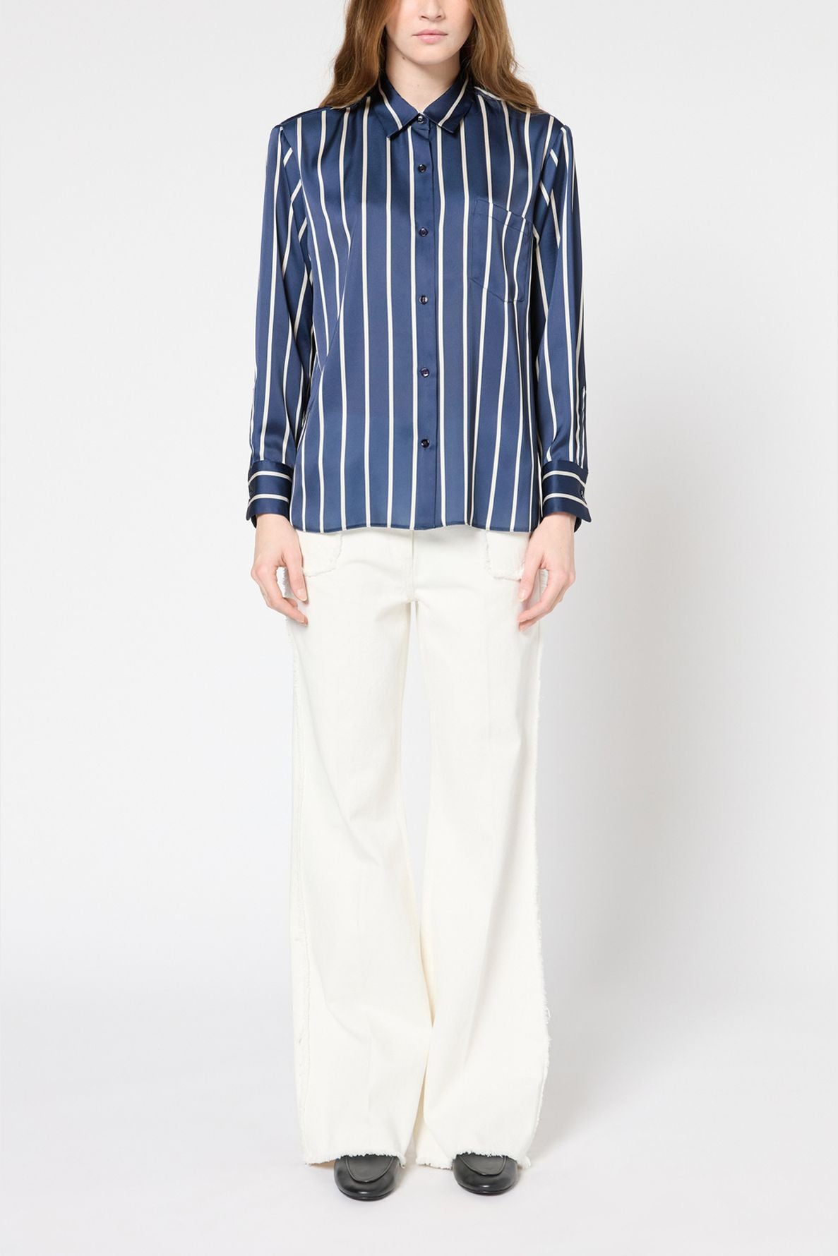 Person wearing a blue and white vertical striped chemise femme with rayures contrastées and wide-leg white pants, standing against a plain white background.