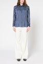 Person wearing a blue and white vertical striped chemise femme with rayures contrastées and wide-leg white pants, standing against a plain white background.