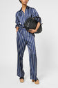 Person wearing a blue and white vertically striped pajama-style chemise femme, carrying a large black bag, and standing in platform sandals against a plain background. The outfit features rayures contrastées for a modern touch.