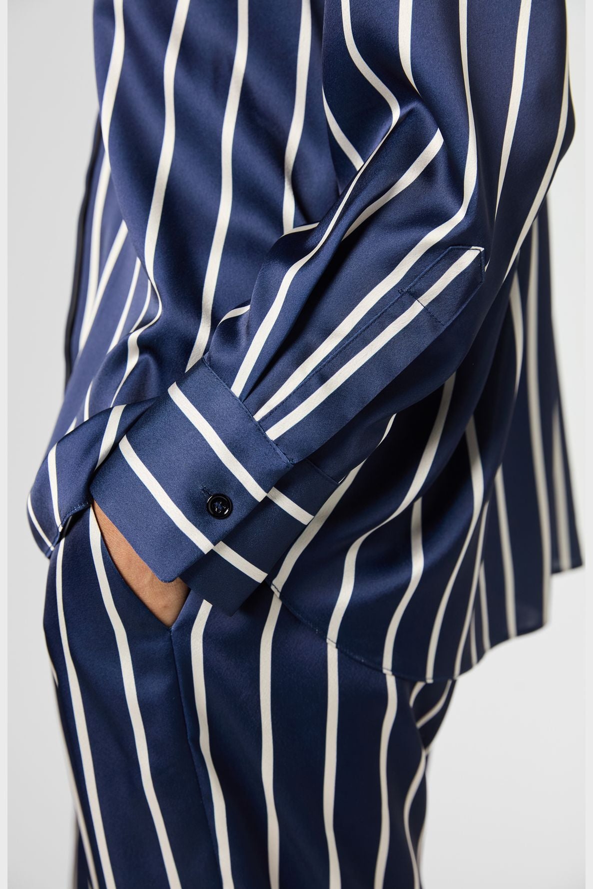 A person wearing a navy blue chemise satinée with rayures contrastées stands sideways with one hand in their pocket.