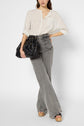 A woman wearing a cream striped blouse, high-waisted gray flared jeans, and platform sandals holds a large black handbag and poses with one hand on her hip against a plain background.