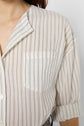 Close-up of a person wearing a light, semi-sheer, collared shirt with vertical black stripes and a chest pocket; the sleeves are rolled up. Only part of the persons face and upper body is visible.