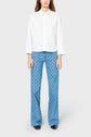 A person wearing a white button-up shirt and high-waisted blue patterned jeans with a flared leg, paired with black shoes, standing against a plain light gray background.