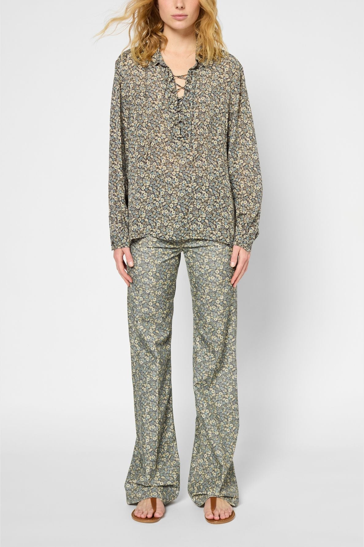A person wearing a loose, long-sleeve chemise à fleurs with an encolure lacée and matching wide-leg floral pants, standing against a plain background for a look that embodies style classique chic.