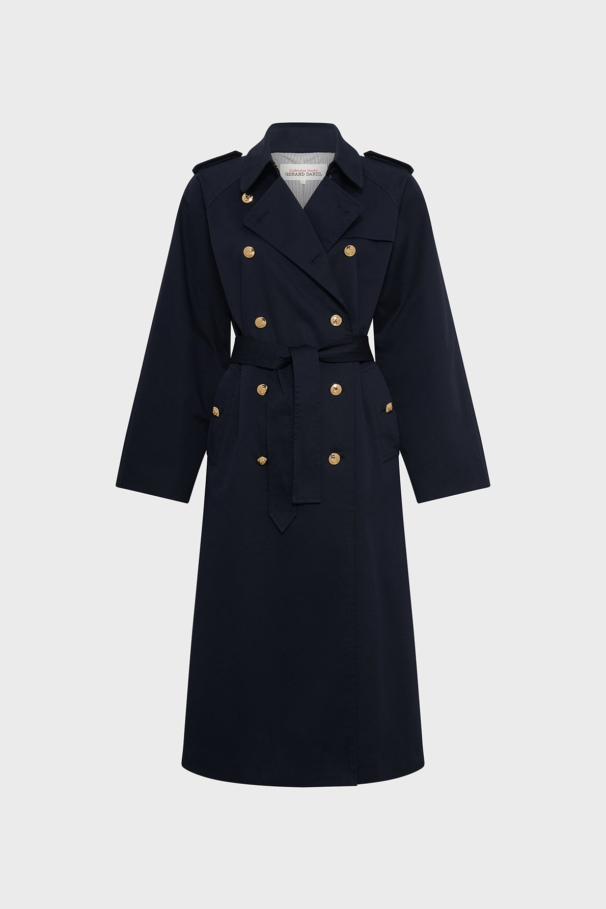 A long, navy blue manteau femme, designed in classic trench long style with double-breasted front, features elegant boutons dorés, a waist belt, and shoulder epaulets—all displayed on a plain light gray background.