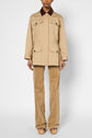 A person stands facing forward wearing a beige coton trench mi-long with a brown col velours côtelé, patterned tan pants, and platform sandals on a plain light background. The person’s head is not visible in the image.