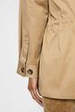 A close-up of a person wearing a light brown trench mi-long jacket with tortoiseshell buttons on the cuff, featuring a col velours côtelé and crafted from soft coton. The image highlights the back and side of the sleeve and hem, with the person’s hand relaxed by their side.