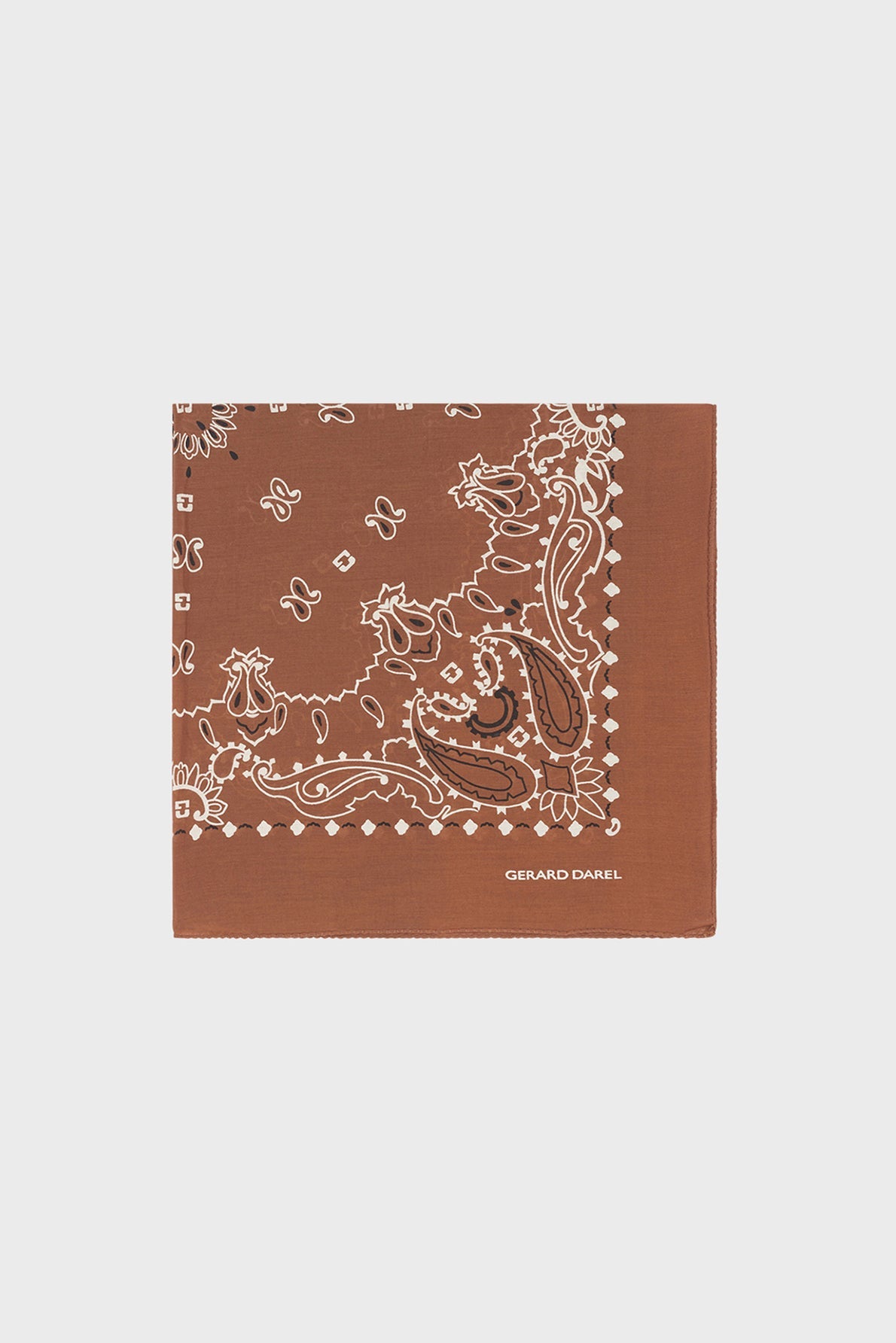 A brown bandana carré in soft coton, featuring a classic white paisley pattern and GERARD DAREL printed in crisp white text in the bottom right corner, displayed on a plain light background. Subtle motifs géométriques add an elegant touch to its timeless design.