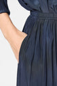 A person wearing a navy blue, pleated skirt or dress with one hand tucked into a side pocket.