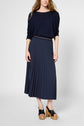 A woman wearing a navy long-sleeve top, a pleated navy midi skirt, and black platform sandals with wooden soles, standing against a plain light background.