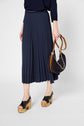 A person wearing a navy pleated midi skirt, black platform sandals with wooden heels, and holding a small navy handbag with brown straps and a gold chain. The background is plain white.