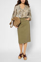 Woman wearing a snakeskin-patterned blouse, olive-green midi skirt, brown platform sandals, and holding a tan suede bag, standing against a plain white background.