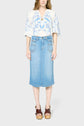 Woman wearing a white blouse with blue floral patterns, a knee-length denim skirt, and brown platform sandals, standing against a plain light background.