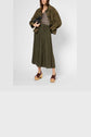 A woman wearing a brown suede jacket, leopard print top, olive green jupe plissée midi skirt, and wooden platform sandals, holding a black clutch.