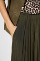 A person wearing an olive green jupe plissée, an animal print top, and an olive blazer stands with one hand in their skirt pocket.