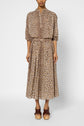 A person wearing a long-sleeved, button-up blouse and a matching jupe imprimé léopard midi skirt, paired with brown platform sandals, stands against a plain white background.