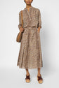 A person wearing a leopard print blouse and a matching jupe imprimé léopard midi skirt stands with hands in pockets. They carry a brown shoulder bag and wear brown platform sandals.
