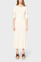 A person wearing a long-sleeved, cream-colored, ribbed midi dress and brown platform sandals stands against a plain light gray background.