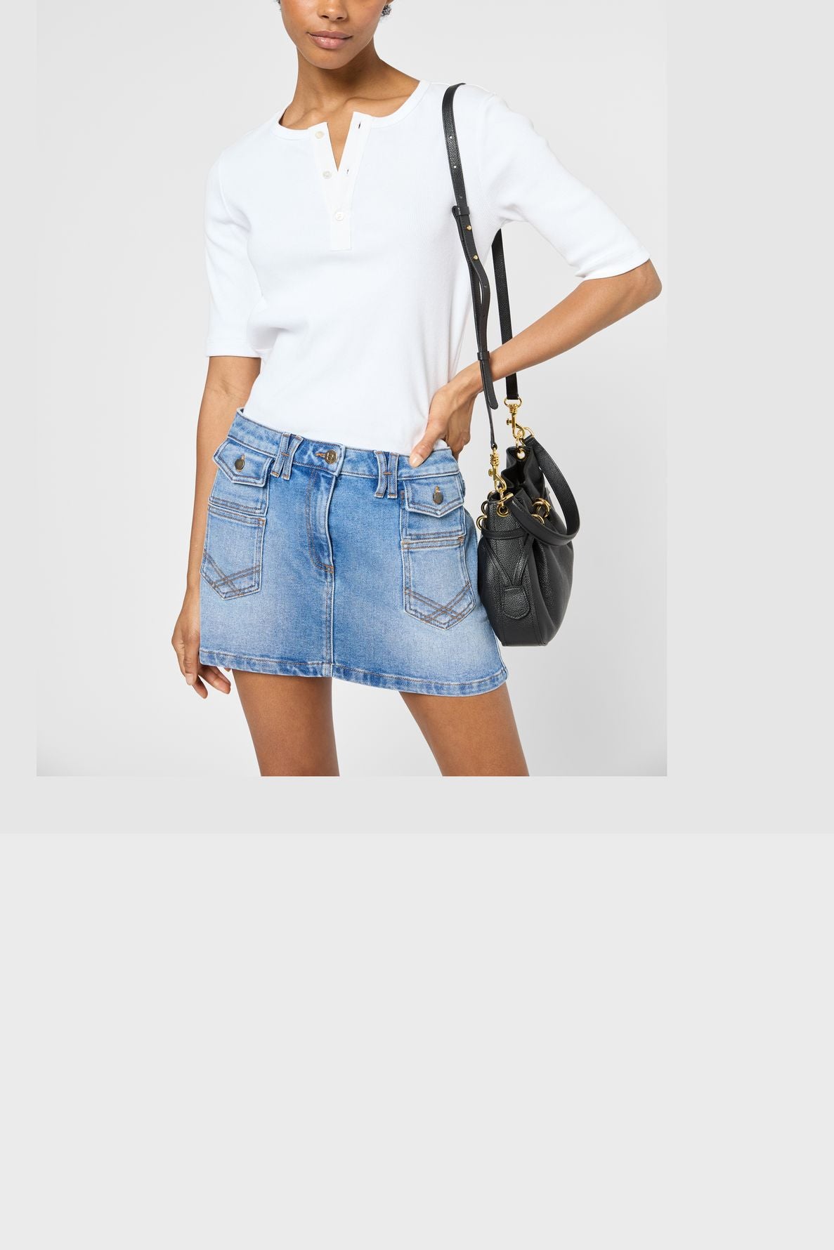 Person wearing a white short-sleeve shirt, mini-jupe en denim bleue, and carrying a black shoulder bag from the collection Studio. The image is cropped at the neck and mid-thigh.