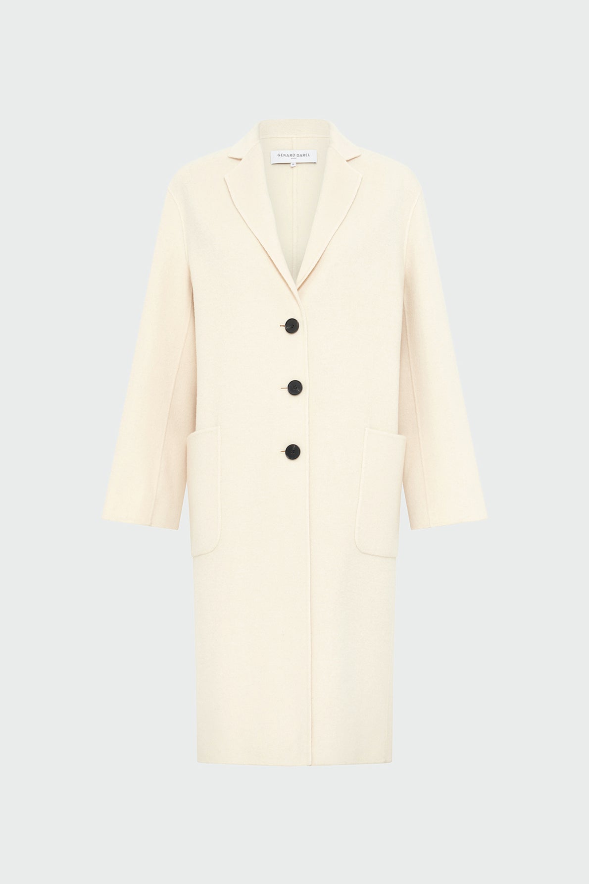 A long, cream-colored manteau droit femme with three black buttons, two large front pockets, and a notched collar, displayed against a light gray background.
