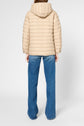 Person standing facing away, wearing a beige doudoune capuche with a hood and blue jeans. The background is plain white.