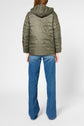 A person wearing a green doudoune capuche puffer jacket and blue flared jeans stands facing away from the camera against a plain white background.