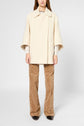 A person wearing a cream-colored, loose-fit manteau coton laine over a light top and beige patterned flared pants featuring subtle motif chevrons, standing against a plain light background. Their face is not visible.