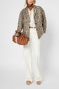 Woman wearing a manteau léopard, white blouse, white pants, tan belt, wedge sandals, brown scarf, and holding a brown handbag. She stands facing forward against a plain background.