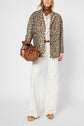 A person wearing a manteau léopard chic, white flared pants, brown platform sandals, a brown belt, and a brown scarf, holding a brown handbag, poses against a plain background.