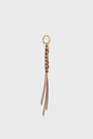 A gold keyring with a brown and beige woven leather tassel in a scoubidou style, featuring long leather strips hanging down—an elegant charm en cuir perfect as an accessoire sac. Photographed on a plain white background.
