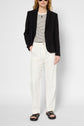 A person wearing a black blazer, striped shirt, and pantalon blanc in coton lyocell lin stands with one hand in their pocket against a plain background, pairing their look with black sandals and sunglasses.