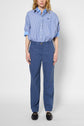 A person wearing a blue and white striped shirt tucked into a pantalon large taille haute in blue lin et lyocell with black loafers stands facing forward against a plain light background.